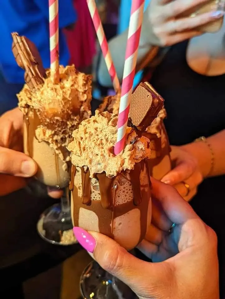 Three loaded Milky Lane thickshakes clinked together across a table · Bueno wafer, chocolate drip and honeycomb crumb